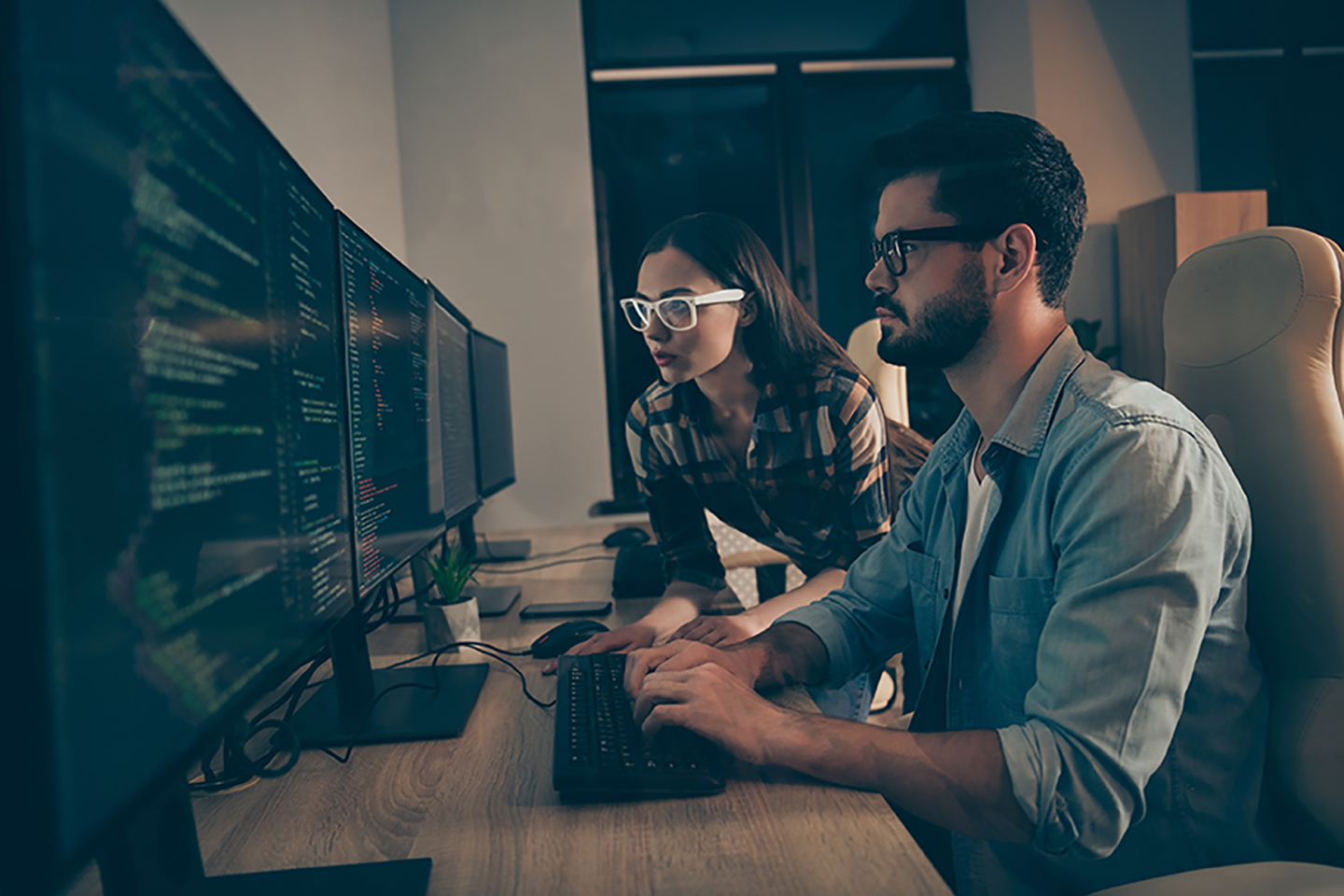 A woman and a man are besida a table. They are looking at a big screen and it seems that they are programming something.