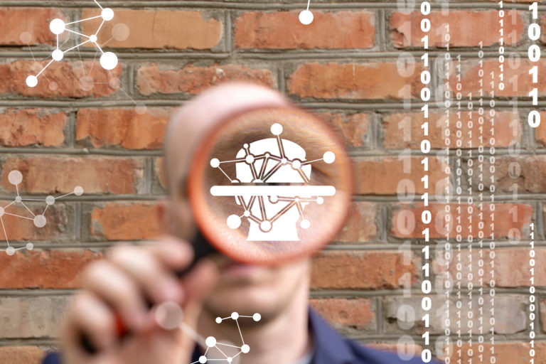 In this picture a man is holding a magnifying glass in front of his face. And the magnifier is showing a digital picture of some kind of head.